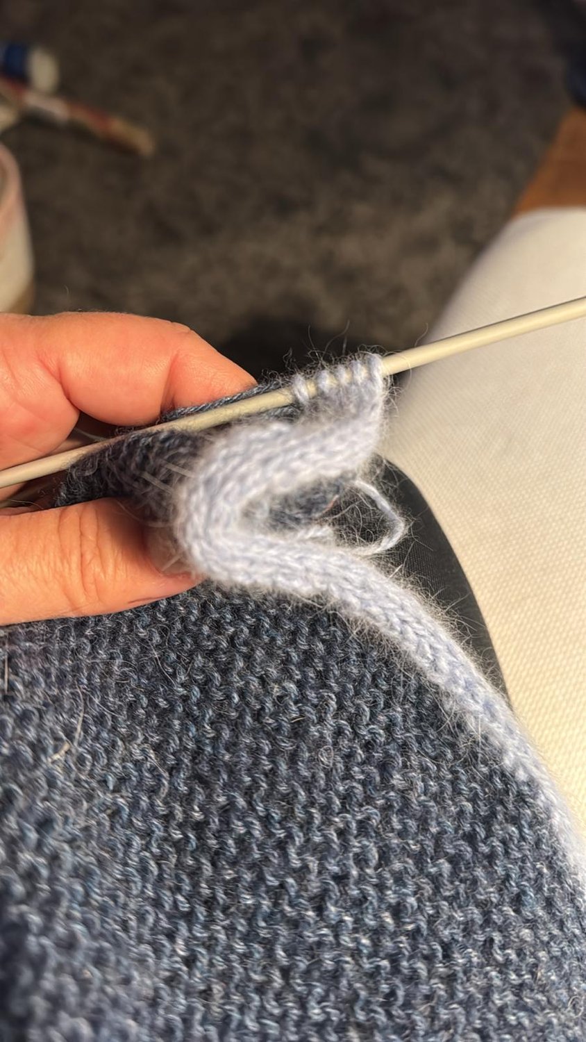Hände beim Stricken eines grauen Wollstücks